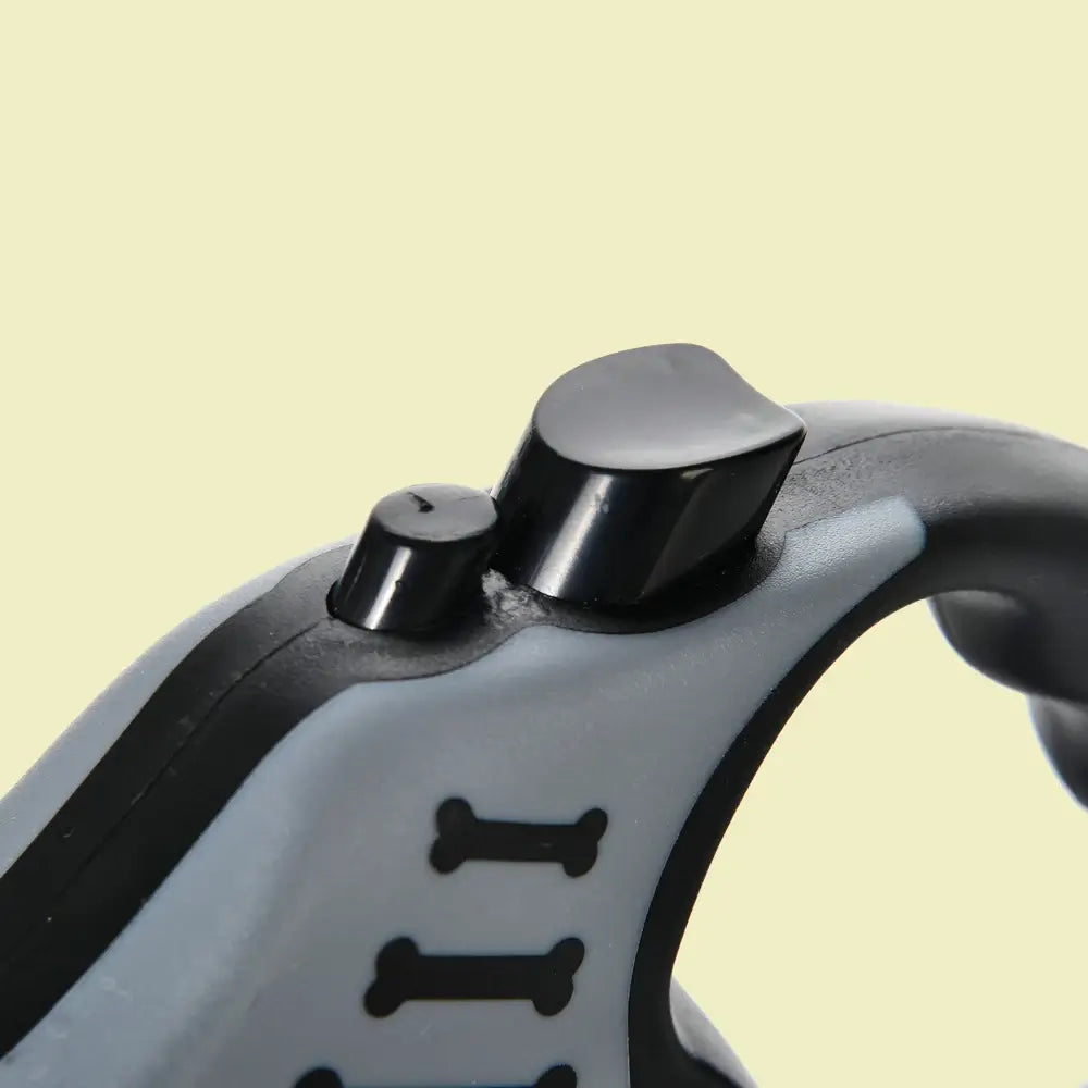 Close-up of dog leash handle showing thumb-lock button and ergonomic black grip with bone detail on beige background