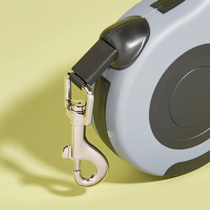 Close-up of retractable dog leash showing durable metal swivel hook and reinforced tape lead connection on yellow background